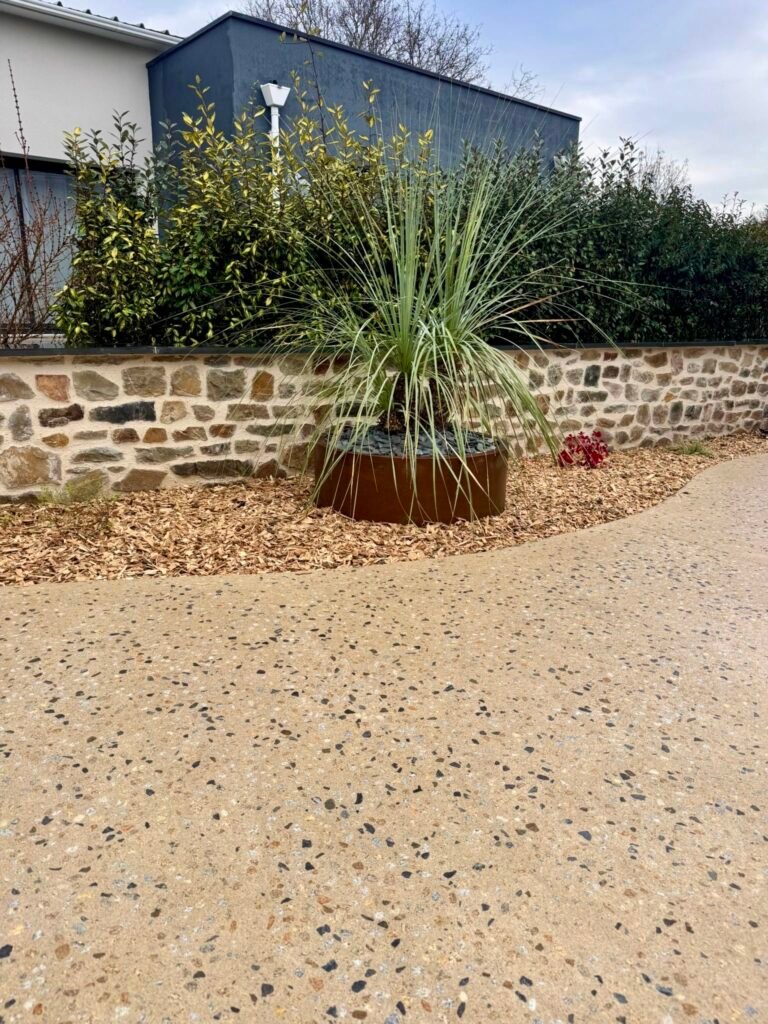 Cour en béton érodé - Muret en pierre avec dessus en ardoirs - jardinières en corten